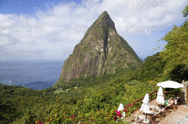 WEST INDIES, St Lucia, Soufriere , Val des Pitons The volcanic plug of Petit Piton and the lush valley seen from the sun deck of the Ladera Spa Resort Hotel with tourists sunbathing on sunbeds beside umbrellas