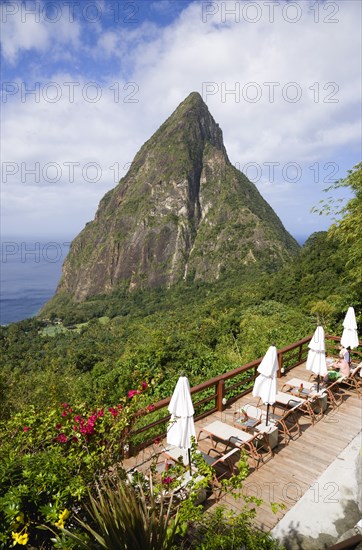 WEST INDIES, St Lucia, Soufriere , Val des Pitons The volcanic plug of Petit Piton and the lush valley seen from the sun deck of the Ladera Spa Resort Hotel with tourists sunbathing on sunbeds beside umbrellas