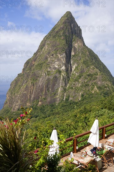 WEST INDIES, St Lucia, Soufriere , Val des Pitons The volcanic plug of Petit Piton and the lush valley seen from the sun deck of the Ladera Spa Resort Hotel with tourists sunbathing on sunbeds beside umbrellas