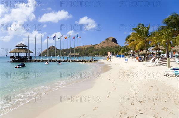 WEST INDIES, St Lucia, Gros Islet , Tourists on the beach at Sandals Grande St Lucian Spa and Beach Resort hotel beside a wooden jetty with Pigeon Island National Historic Park beyond