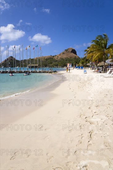 WEST INDIES, St Lucia, Gros Islet , Tourists on the beach at Sandals Grande St Lucian Spa and Beach Resort hotel beside a wooden jetty with Pigeon Island National Historic Park beyond