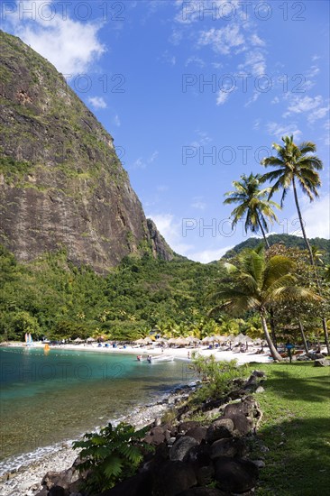 WEST INDIES, St Lucia, Soufriere , Val des Pitons The white sand beach at the Jalousie Plantation Resort Hotel with the volcanic plug of Petit Piton beyond and tourists on sunbeds beneath palapa sun shades