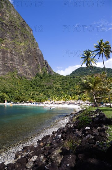 WEST INDIES, St Lucia, Soufriere , Val des Pitons The white sand beach at the Jalousie Plantation Resort Hotel with the volcanic plug of Petit Piton beyond and tourists on sunbeds beneath palapa sun shades