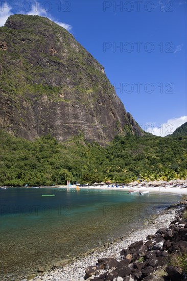 WEST INDIES, St Lucia, Soufriere , Val des Pitons The white sand beach at the Jalousie Plantation Resort Hotel with the volcanic plug of Petit Piton beyond and tourists on sunbeds beneath palapa sun shades