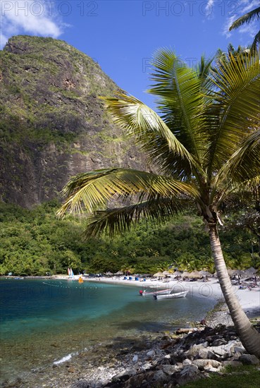 WEST INDIES, St Lucia, Soufriere , Val des Pitons The white sand beach at the Jalousie Plantation Resort Hotel with the volcanic plug of Petit Piton beyond and tourists on sunbeds beneath palapa sun shades