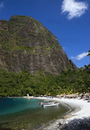 WEST INDIES, St Lucia, Soufriere , Val des Pitons The white sand beach at the Jalousie Plantation Resort Hotel with the volcanic plug of Petit Piton beyond and tourists on sunbeds beneath palapa sun shades