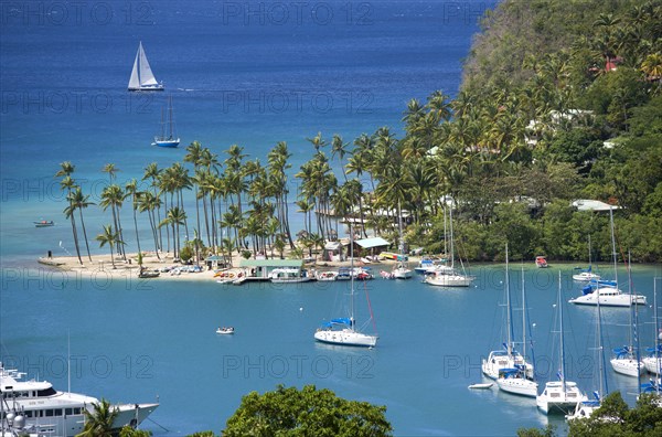 WEST INDIES, St Lucia, Castries , Marigot Bay The harbour with yachts at anchor and a yacht sailing out at sea beyond the small coconut palm tree lined beach of the Marigot Beach Club sitting at the entrance