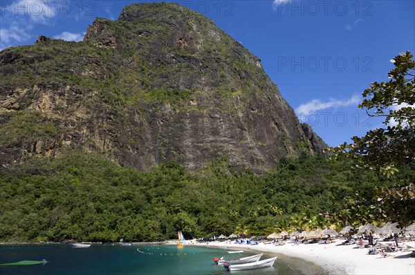 WEST INDIES, St Lucia, Soufriere , Val des Pitons The white sand beach at the Jalousie Plantation Resort Hotel with the volcanic plug of Petit Piton beyond and tourists on sunbeds beneath palapa sun shades