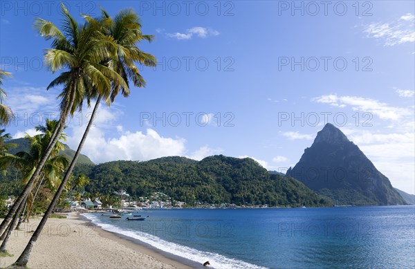 WEST INDIES, St Lucia, Soufriere, Soufriere beach lined with coconut palm trees with the town and the volcanic plug mountain of Petit Piton beyond
