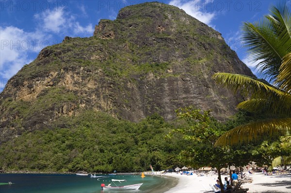 WEST INDIES, St Lucia, Soufriere , Val des Pitons The white sand beach at the Jalousie Plantation Resort Hotel with the volcanic plug of Petit Piton beyond and tourists on sunbeds beneath palapa sun shades