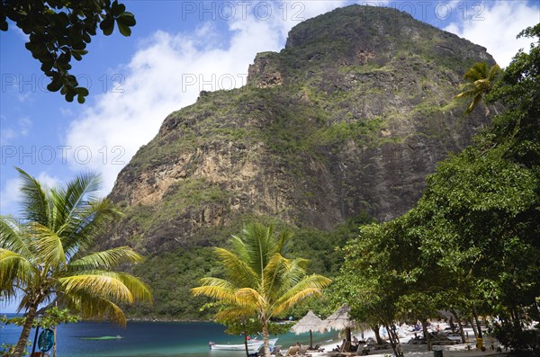 WEST INDIES, St Lucia, Soufriere , Val des Pitons The white sand beach at the Jalousie Plantation Resort Hotel with the volcanic plug of Petit Piton beyond and tourists on sunbeds beneath palapa sun shades