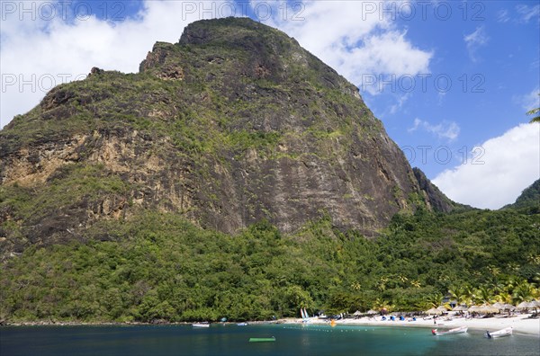 WEST INDIES, St Lucia, Soufriere , Val des Pitons The white sand beach at the Jalousie Plantation Resort Hotel with the volcanic plug of Petit Piton beyond and tourists on sunbeds beneath palapa sun shades