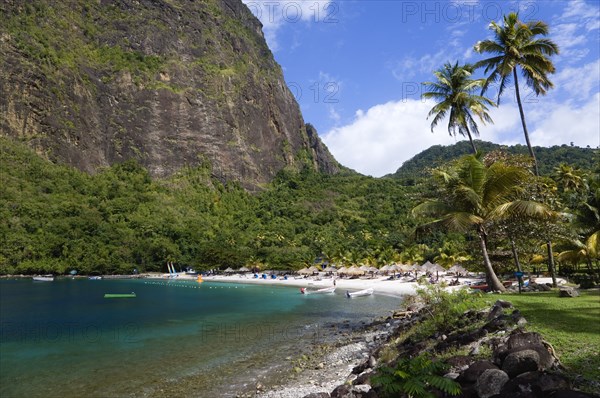 WEST INDIES, St Lucia, Soufriere , Val des Pitons The white sand beach at the Jalousie Plantation Resort Hotel with the volcanic plug of Petit Piton beyond and tourists on sunbeds beneath palapa sun shades