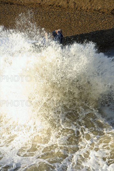 ENGLAND, East Sussex, Brighton, Waves crashing onto beach and groyne with people getting wet.