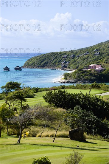 WEST INDIES, St Vincent & The Grenadines, Canouan, Raffles Resort Trump International Golf Course designed by Jim Fazio. The 7th fairway and 6th green with the pink Villa Juliet and Amrita Spa beyond on Godahl beach