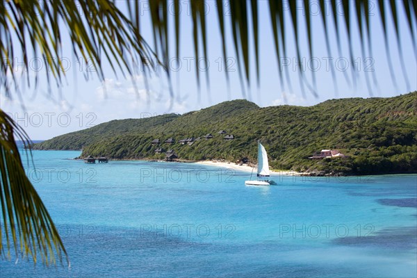 WEST INDIES, St Vincent & The Grenadines, Canouan, Raffles Resort Hotel with a catamaran leaving Carenage Bay passing the pink Villa Juliet and the Amrita Spa on Godahl Beach