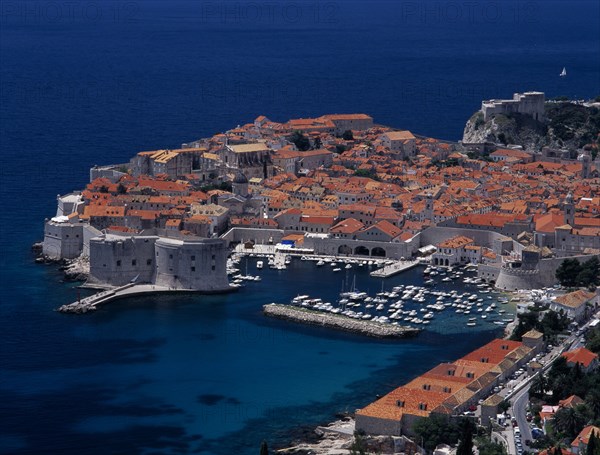 CROATIA, Dalmatia, Dubrovnik, Elevated view over the Old City Harbour with fortified walls. Yachts moored in marina surrounded by buildings with terracotta tiled rooftops