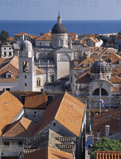 CROATIA, Dalmatia, Dubrovnik, "Elevated view across terracotta tiled roof tops in the Old City towards the Cathedral, known as the Church of the Assumption. Seen in evening light with the ocean behind "