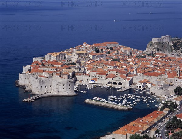 CROATIA, Dalmatia, Dubrovnik, Elevated view over the Old City Harbour with fortified walls. Yachts moored in marina surrounded by buildings with terracotta tiled rooftops