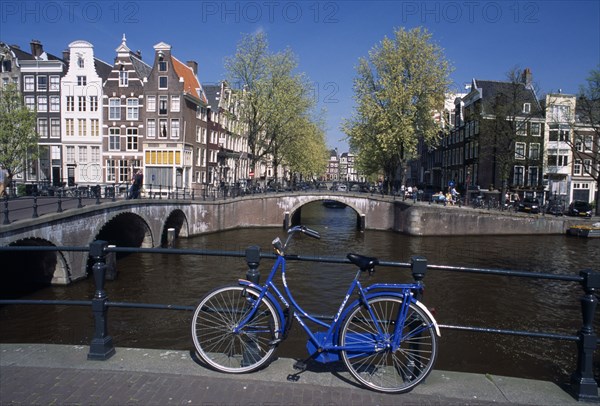 HOLLAND, Noord Holland, Amsterdam, Blue bicycle leaning against a railing on bridge with Keizergracht Canal running parallel and Leidsegracht perpendicular. Traditional waterside house facades behind.