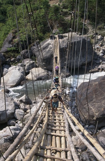NEPAL, Annapurna Circuit Trek, Crossing a sagging suspension bridge over the Khudi Khola at Khudi. Bridge made from woode with metal support wires.