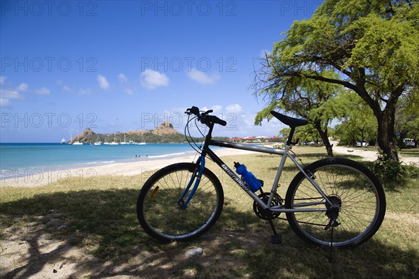 WEST INDIES, St Lucia, Gros Islet , Pigeon Island National Historic Park seen from a nearby beach on a causeway to the island with yachts at anchor in Rodney Bay and a parked mountain bike in the foreground