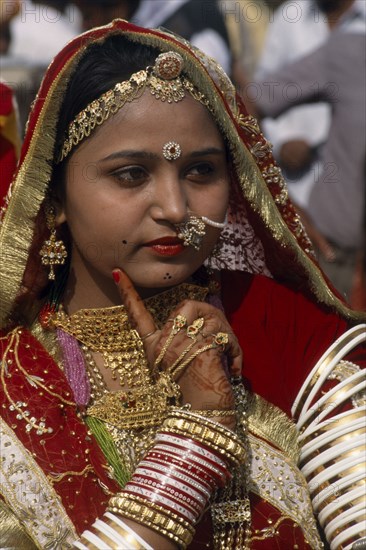 INDIA, Rajasthan, Jaisalmer, "Portrait of a Miss Desert contestant with henna painted hands, finger resting on her cheek. Wearing red and gold with traditional jewellery at the Desert Festival"