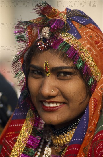 INDIA, Rajasthan, Alwar, Portrait of a female dancer smiling wearing a multi coloured head dress at the Alwar Utsav Festival