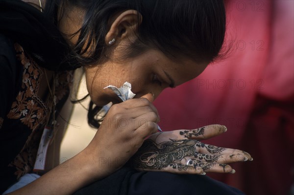 INDIA, Rajasthan, Alwar, Participant in the Mehendi competition at the Alwar Utsav Festival applying an intricate henna design onto the palm of her hand
