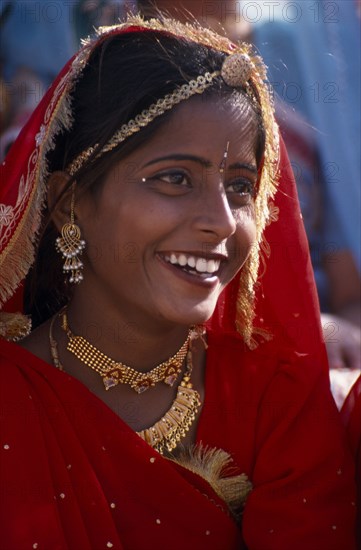 INDIA, Rajasthan, Bikaner, Portrait of a girl dancer smiling wearing red and gold at the Camel Festival