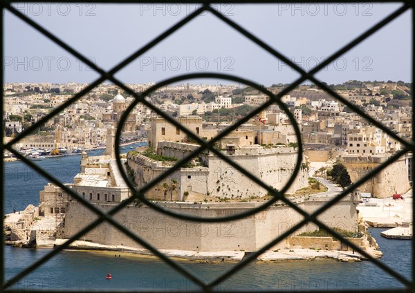 MALTA, Valletta, Fort Saint Angelo on Vittoriosa one of the Three Cities in Valletta Harbour seen through the metal railings of the Upper Barrakka Gardens in Valletta