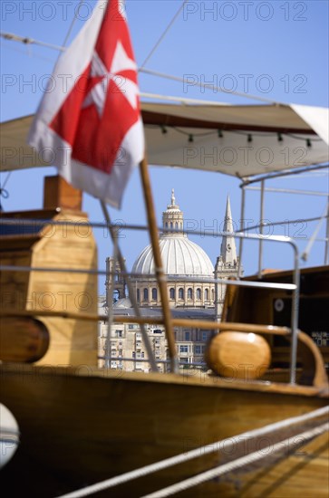 MALTA, Valletta, The dome of the Carmelite Church of 1573 seen through the foredeck of an old schooner with a Maltese Cross flag moored on Sliema waterfront
