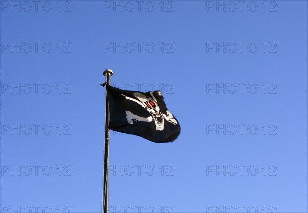 ENGLAND, East Sussex, Hastings, Skull and cross bones pirate flag flying against a blue sky
