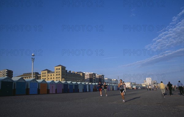 ENGLAND, East Sussex, Brighton, Joggers on Hove Lawns Esplanade by colourful beach huts in late afternoon sunshine.