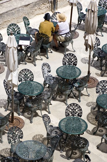 MALTA, Valletta, Couple of people sitting at a table amongst other wrought iron tables and chairs in a cafe below the Upper Barrakka Gardens overlooking Valletta Harbour