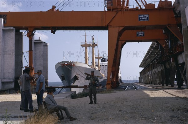 CUBA, Industry, Soldiers in dockyard with container ship moored behind framed by huge steel crane.