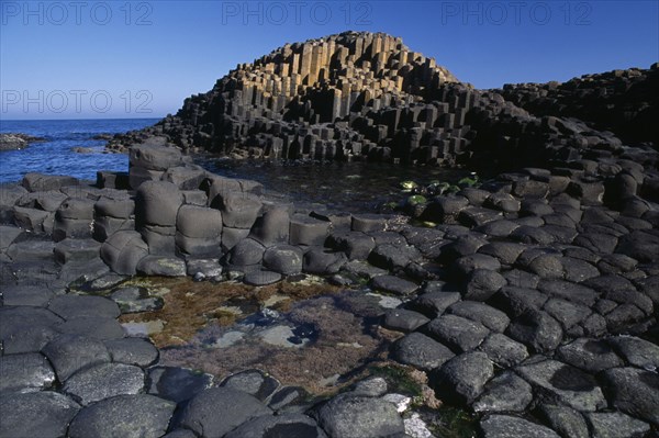 NORTHERN IRELAND, Co Antrim, Giants Causeway, Interlocking basalt stone columns left by volcanic eruptions. View across the main and most visited section of the causeway with the coastline seen behind.