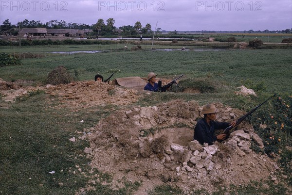 VIETNAM, War, "North Vietnamese combat troops, positioned with rifles and machine gun in dug-outs with paddy fields and workers behind."