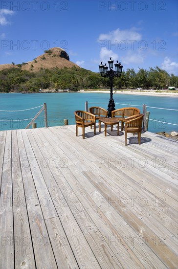 WEST INDIES, St Lucia, Gros Islet , Signal Hill on Pigeon Island National Historic Park seen from a nearby wooden jetty with a table and chairs beside a wrought iron lamppost