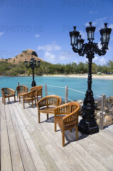 WEST INDIES, St Lucia, Gros Islet , Signal Hill on Pigeon Island National Historic Park seen from a nearby wooden jetty with a table and chairs beside a wrought iron lamppost