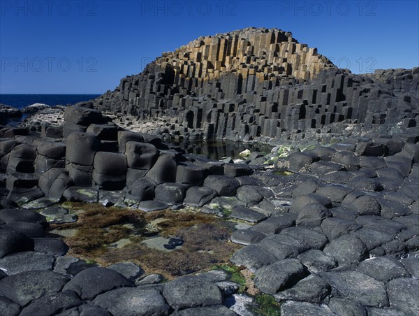 NORTHERN IRELAND, County Antrim, Giants Causeway, Interlocking basalt stone columns left by volcanic eruptions. View across the main and most visited section of the causeway with the coastline seen behind.