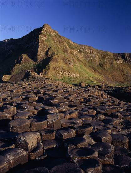 NORTHERN IRELAND, County Antrim, Giants Causeway, Interlocking basalt stone columns left by volcanic eruptions. View towards the south from the main section seen in golden light.