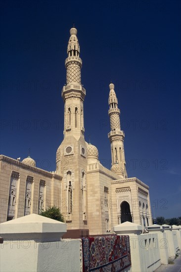 UAE, Dubai, Jumeirah Mosque.  Angled view of exterior with pair of minarets and domed rooftop decorated with hexagonal pattern.  Carpet lying over white wall in foreground.