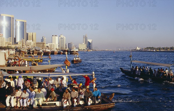 UAE, Dubai, Dubai Creek, Abra water taxis with passengers on Creek with city skyline beyond.