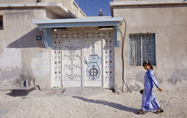 UAE, Dubai, Bur Dubai , Young girl passing building with carved and decorated doorway.  Sheikh Zayed Road behind.