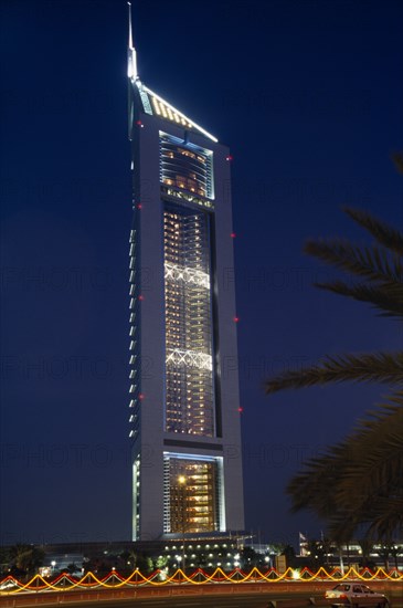UAE, Dubai , Emirates Tower illuminated at night with coloured lights and passing car in the foreground.