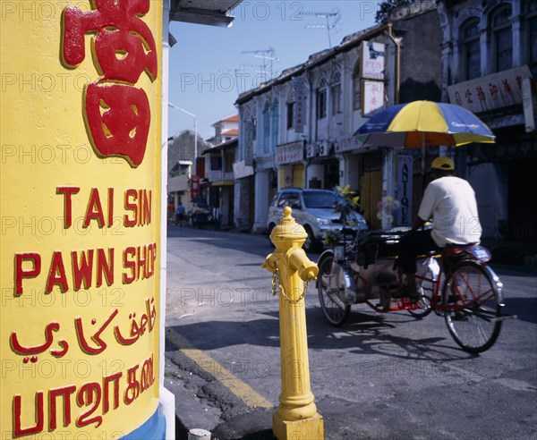 MALAYSIA, Penang, Georgetown, Lebuh Chulia.  Cycle rickshaw on street with yellow and red painted sign for pawn shop written in four different languages in immediate foreground.