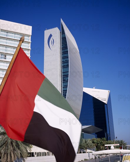 UAE, Dubai, National Bank of Dubai seen from dhow on Dubai creek with UAE flag in the foreground.