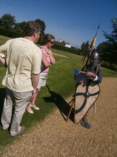 ENGLAND, East Sussex, Battle, "Battle Abbey. Visitors in grounds of partially ruined abbey complex, talking to a foot soldier near to the spot that King Harold fell in the 1066 Battle of Hastings"