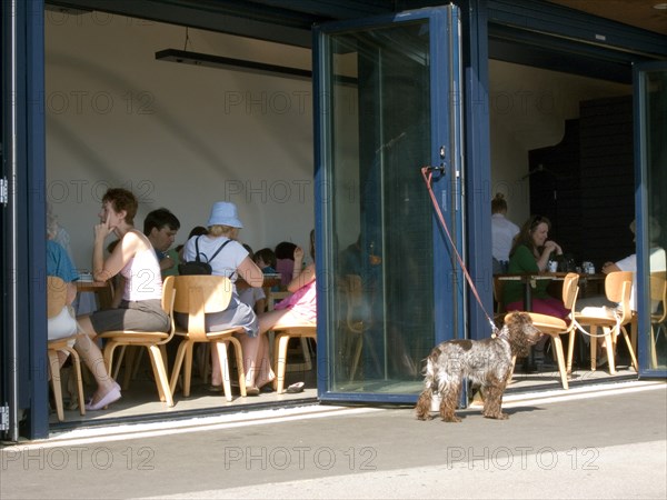 ENGLAND, West Sussex, Littlehampton, Customers sitting at tables inside the East Beach Cafe designed by Thomas Heatherwick. Dog tied to glass door waiting outside